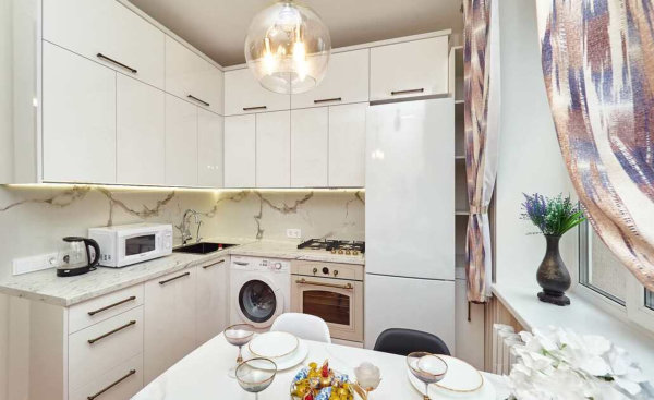 Белая мебель, мраморный фартук, сервированный стол и фиолетовые цветы на подоконнике.