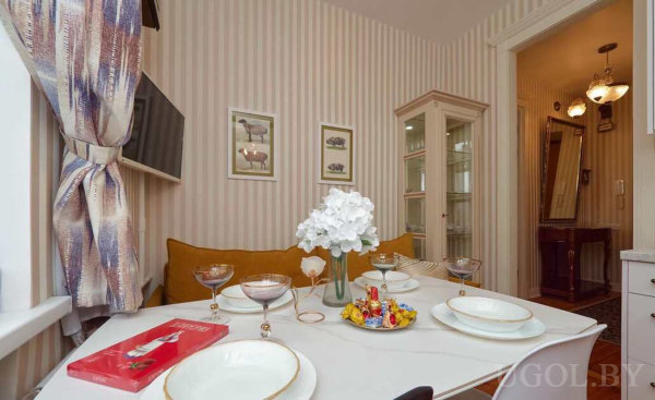 Сервированный стол на четверых, белые тарелки с золотым кантом, конфеты и цветы в центре.