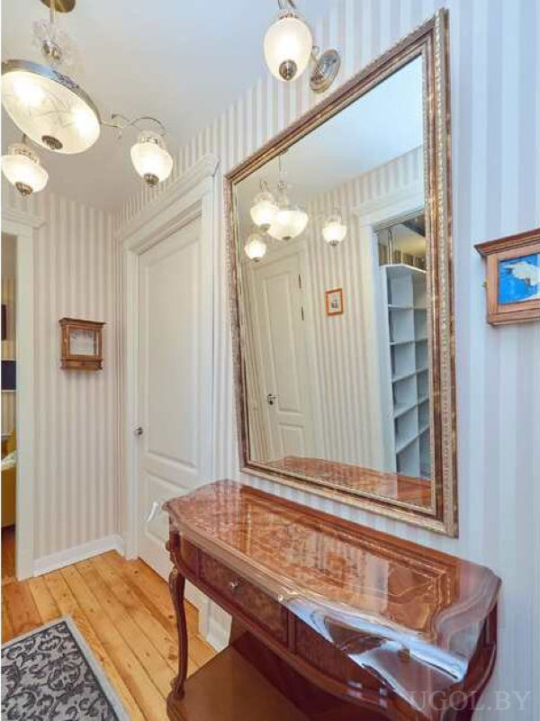 Полосатые обои, деревянная консоль, большое зеркало в золотой раме и декоративные светильники.