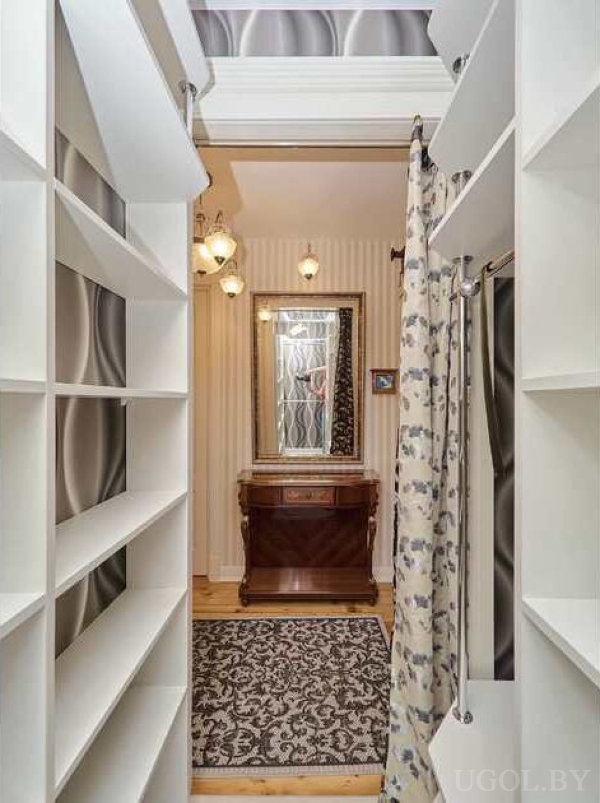 Белые полки для обуви, цветочная штора, зеркало и комод в комнате с полосатыми обоями и ковром.
