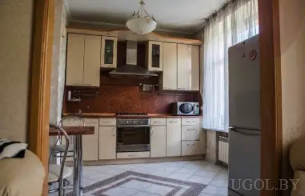 Современная кухня с U-образной планировкой, светлыми фасадами, барной стойкой и металлическими стульями. Встроенная техника, декоративный фартук и большое окно с тюлем создают уютную атмосферу.