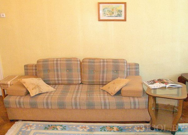 Комната с клетчатым диваном, декоративными подушками, стеклянным столиком с книгой и ковром с узором.