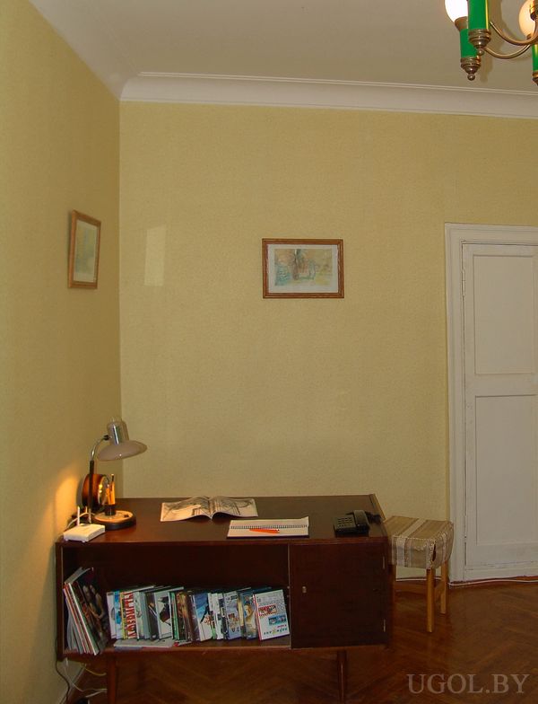 Комната с письменным столом у жёлтой стены, книгами и лампой, открытой книгой и стулом с полосатой подушкой.