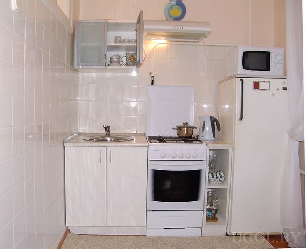 Компактная кухня с белыми шкафами, плитой, мойкой, красным холодильником и микроволновкой.