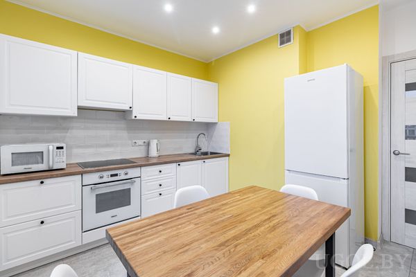 Кухня с белыми фасадами, деревянной столешницей, жёлтыми стенами и столом с белыми стульями.