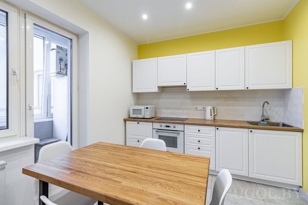 Кухонная зона с белыми шкафами, деревянной столешницей, жёлтой стеной и выходом на балкон.