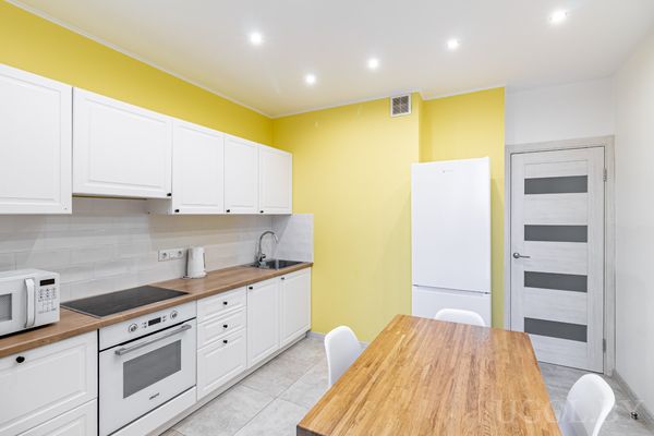 Кухня с белыми фасадами, плитой, холодильником и жёлто-белыми стенами в современном стиле.