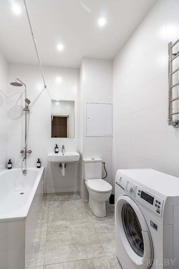 Компактная ванная с белой сантехникой, стиральной машиной и настенным полотенцесушителем.