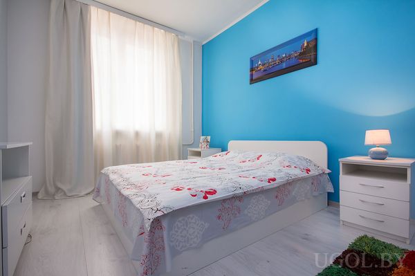 Комната с ярко‑синей стеной, белой кроватью и покрывалом с красно‑серым цветочным узором.