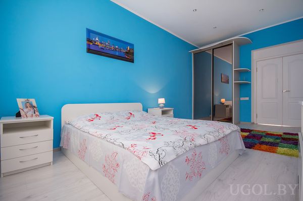 Современная спальня с белой кроватью, зеркальным шкафом и фотографией города над изголовьем.