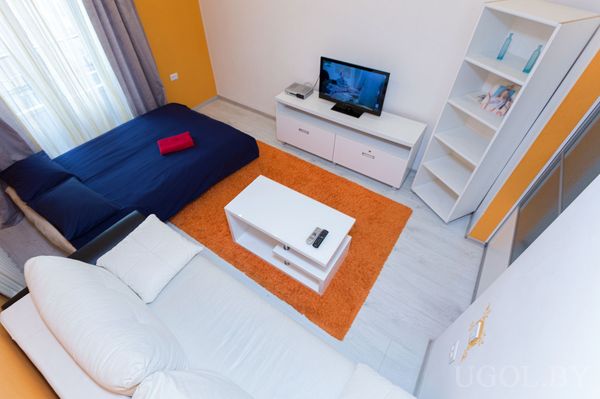 Интерьер с белым диваном, журнальным столиком, тёмно‑синей кроватью‑днём и телевизором на белой тумбе.