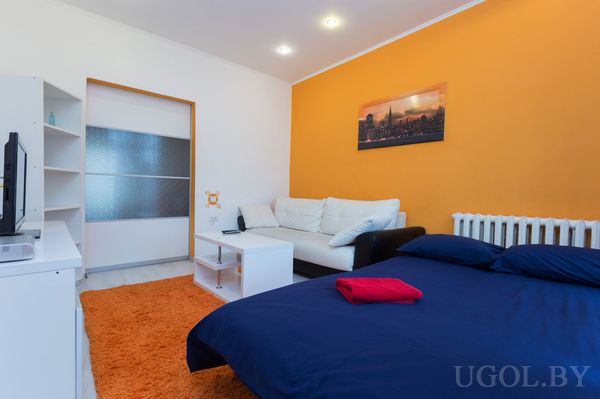 Комната с диваном, белым столиком, тёмно‑синей кроватью и телевизионной зоной; видна раздвижная дверь.