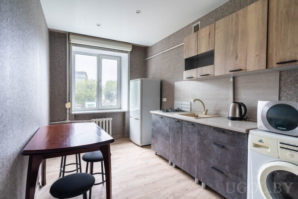 Кухня с плитой, мойкой и холодильником, барная стойка с табуретами, окно с видом на зелень.