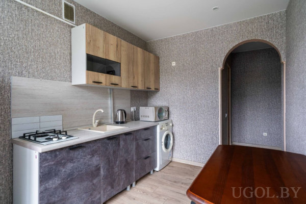 Плита, мойка, микроволновка и стиральная машина, деревянные шкафы, арочный проход и стол.