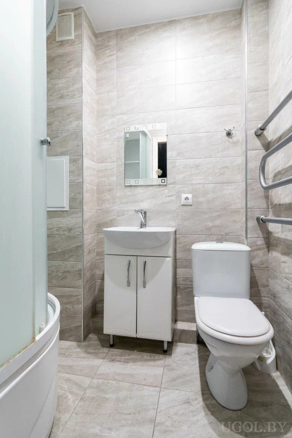 Душ с изогнутой дверью, раковина с зеркалом, унитаз, серые плитки и полотенцесушитель.