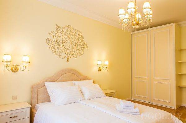 Элегантная спальня с большой кроватью, мягким изголовьем, белым бельём, сложенными полотенцами и настенными светильниками.