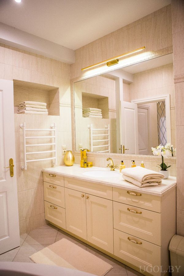 Современная ванная с белой тумбой, большим зеркалом, полотенцесушителем и аккуратно разложенными аксессуарами.