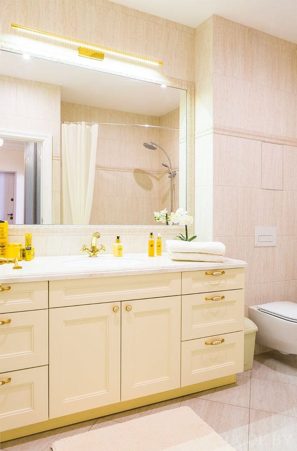Светлая ванная с белой тумбой, зеркалом, унитазом и жёлтыми аксессуарами на столешнице.
