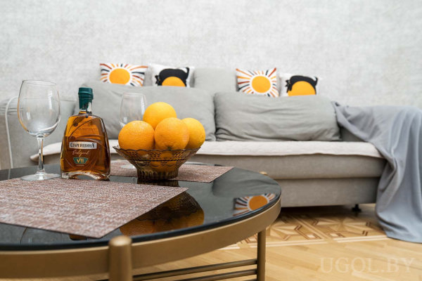 Стеклянный стол, диван с подушками «пингвин» и «солнце», теплый деревянный пол.