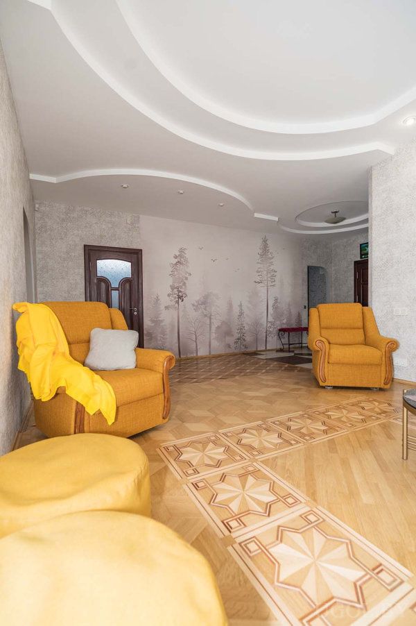 Мистический лес на стене, кресла с деревянными подлокотниками и геометрический паркет.