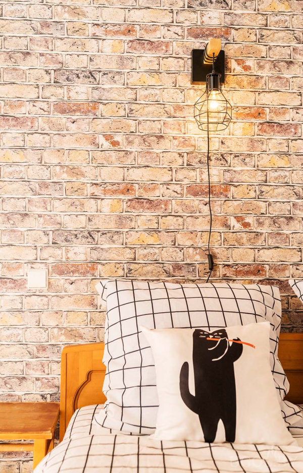 Кирпичная стена, геометрический светильник и белое постельное бельё с черной сеткой.