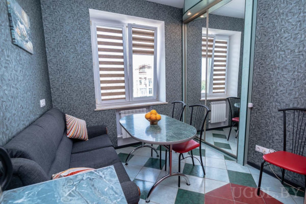 Мраморный стол, серый угловой диван, зеркальный шкаф и зебра-жалюзи на окнах.