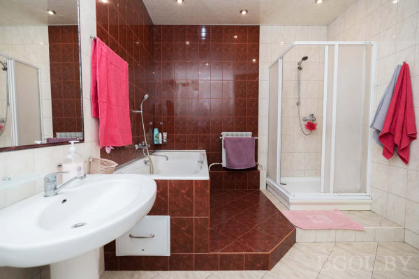 Белая раковина, ванна, стеклянная душевая и яркие полотенца на стенах.