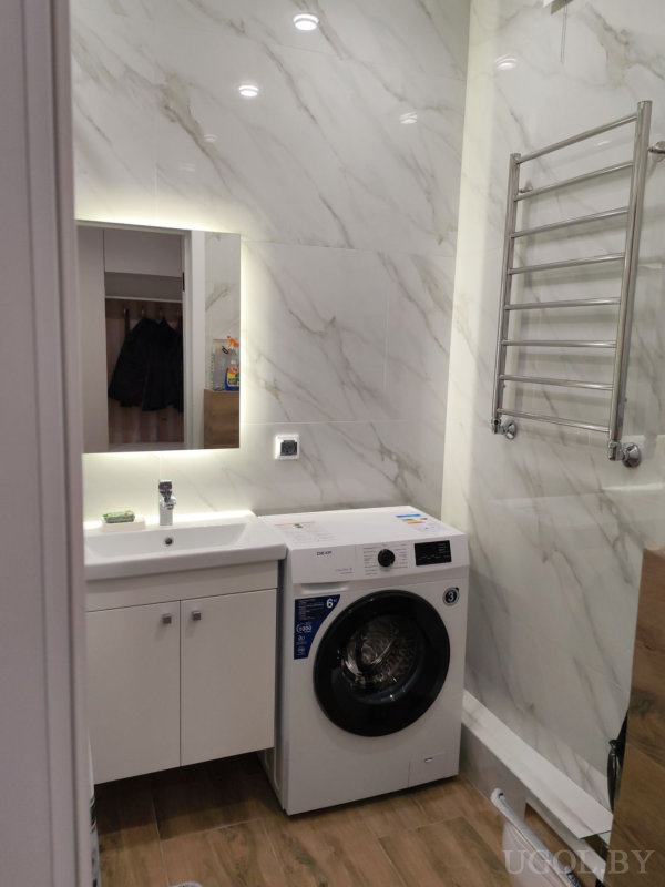 Ванная комната с белой плиткой, деревянным полом, зеркалом с подсветкой и стиральной машиной.