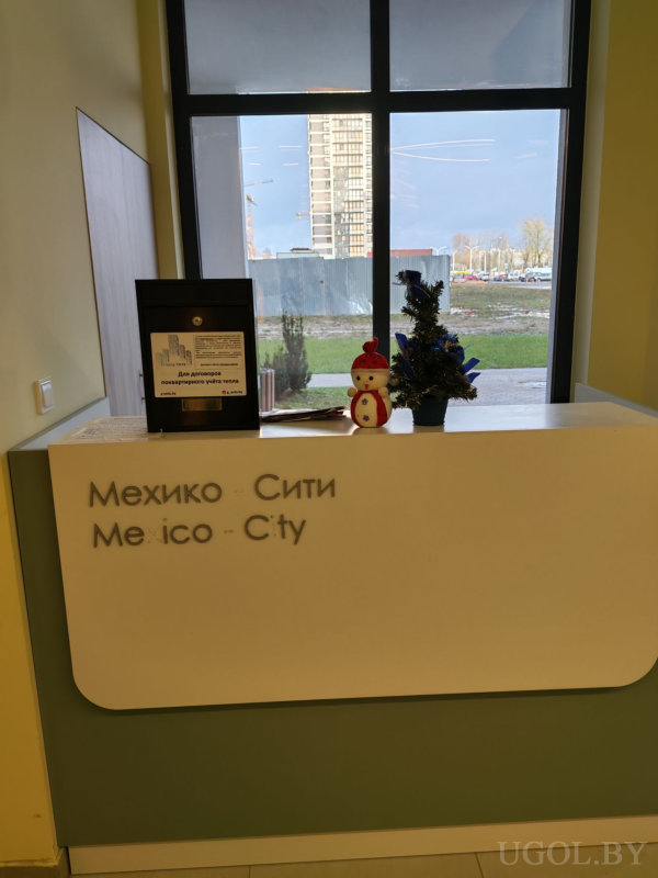 Стойка с надписью «Мехико Сити», мини-ёлкой и видом на стройку за окном.