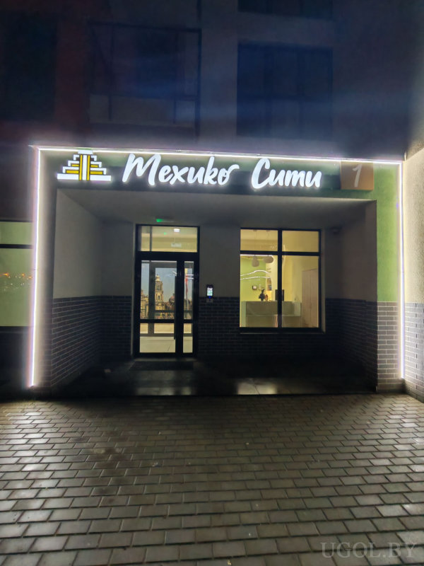 Освещённый вход с надписью «Мехико Сити», стеклянной дверью и видимым ресепшеном внутри.