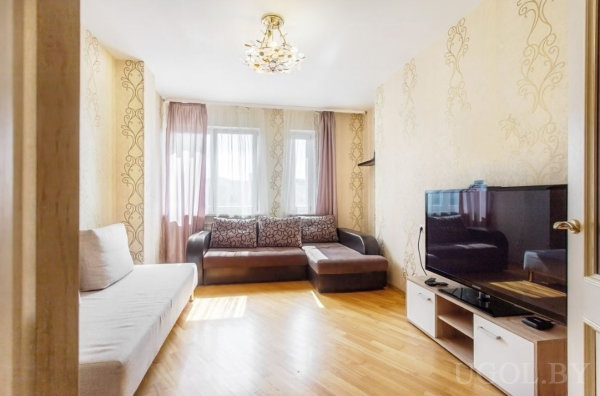 Современная уютная гостиная с бежевым и коричневым диванами, светлым полом и декоративными шторами.