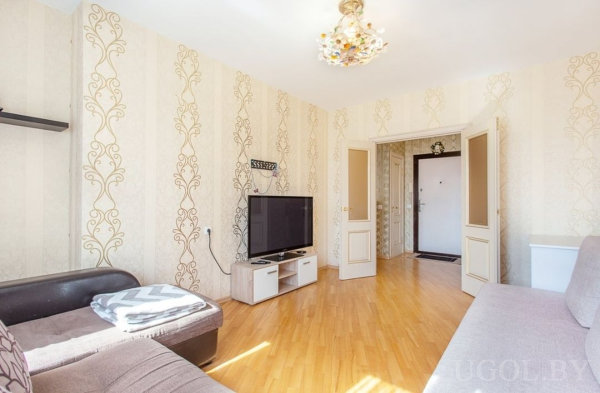 Светлая комната с двумя диванами, узорчатыми обоями, телевизором на тумбе и видом на прихожую.