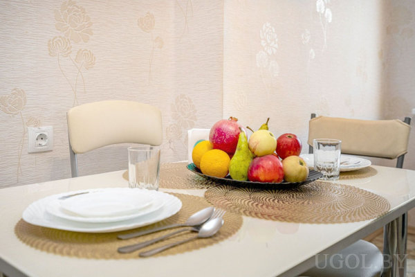 Небольшой стол с двумя сервировками и вазой с гранатами, апельсинами, грушами, яблоками и бананами.
