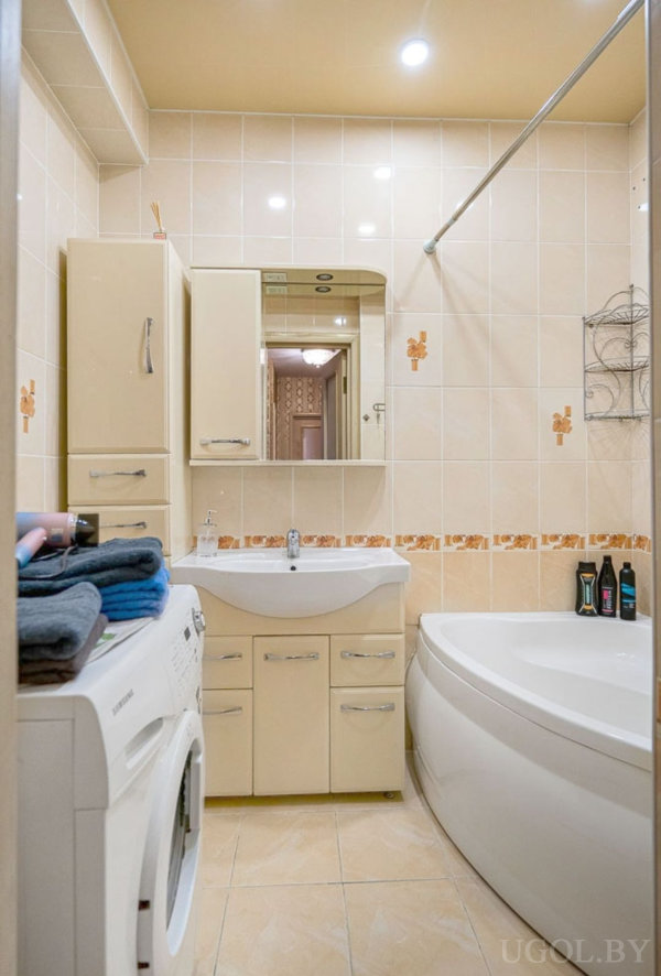Компактная ванная с бежевой плиткой, белой раковиной, зеркалом и стиральной машиной.