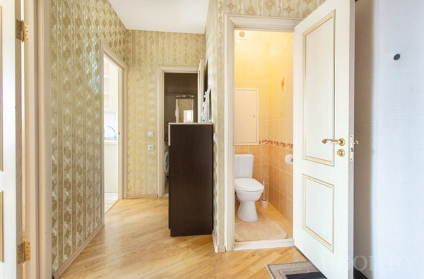 Жилой коридор с дверями в ванную, прачечную и кухню, светлыми обоями и деревянным полом.