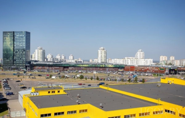 Вид на город с желтым зданием на переднем плане, парковкой и высотками на фоне.