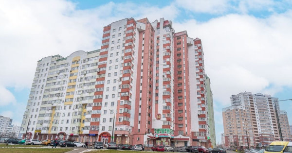 Жилой район с домами в красно-белых тонах, магазинами, припаркованными машинами и прохожими.