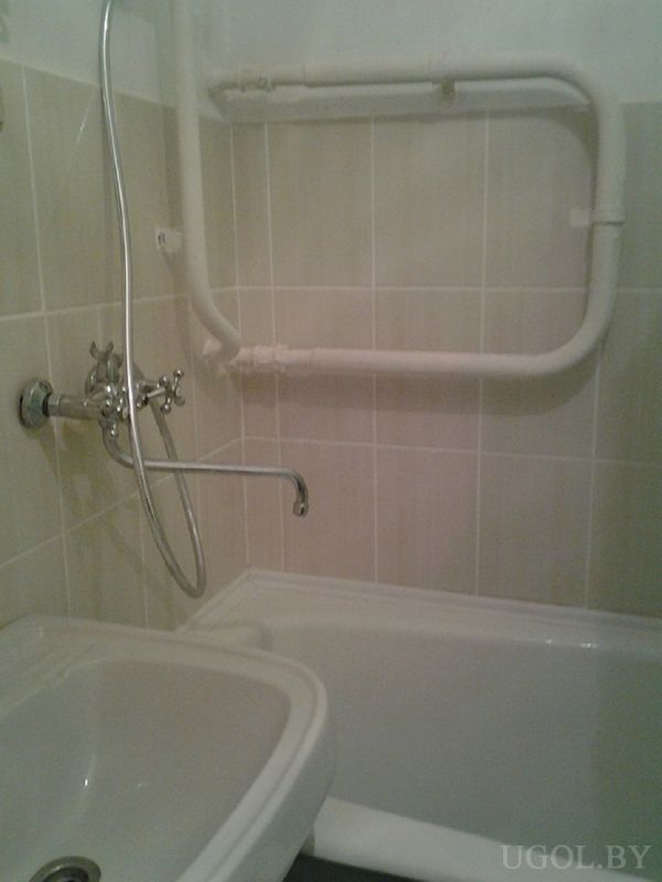 Компактная ванная с белой ванной, умывальником, настенным полотенцесушителем и светлой плиткой.