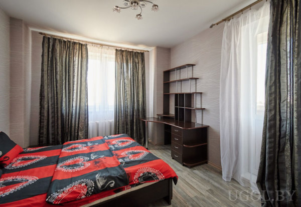 Комната с двуспальной кроватью в черно-красных тонах, двумя окнами и письменным столом у стены.