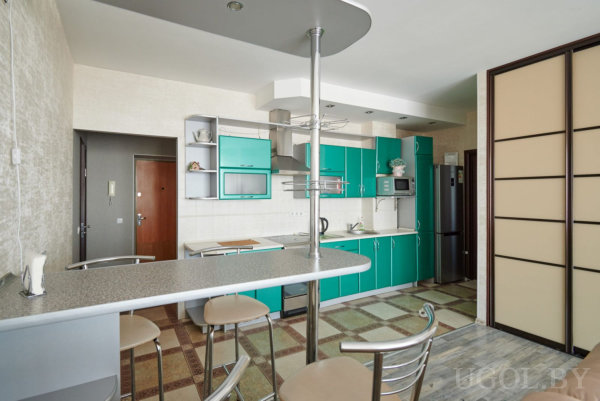 Современная кухня с белыми столешницами, встроенной техникой и барными стульями у изогнутой стойки.