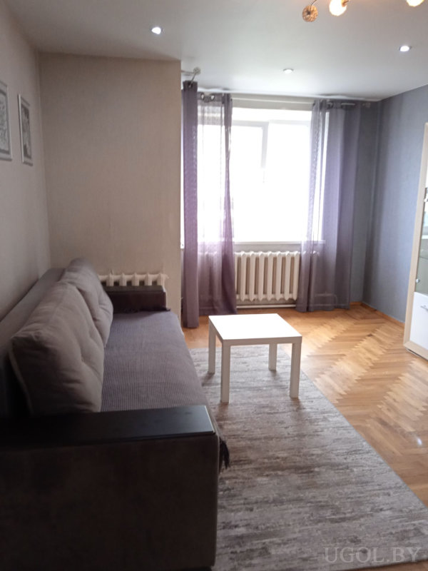 Серый диван, белый столик, светлый ковер и окно с прозрачными шторами создают уютную атмосферу.