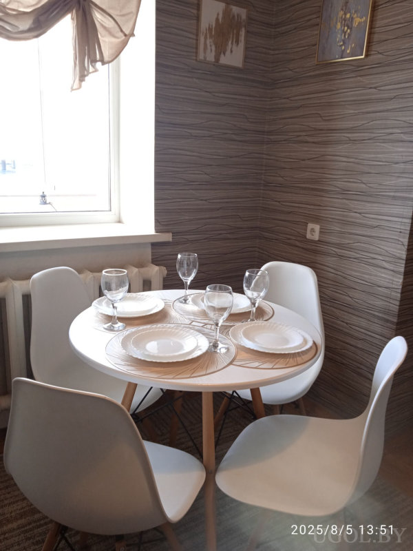 Круглый стол с белыми тарелками и бокалами, четыре современные стула и абстрактные картины на стене.