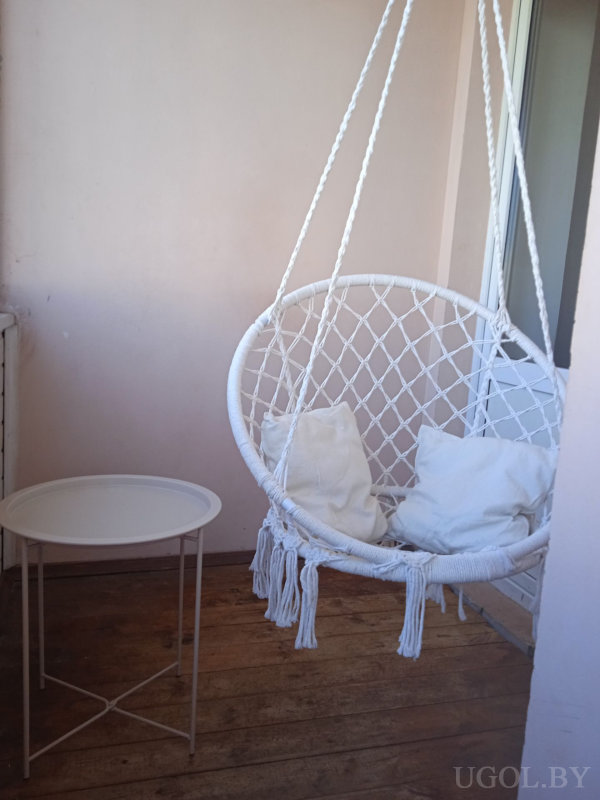 Белое плетёное кресло с подушками, маленький столик и светло-розовые стены создают атмосферу отдыха.