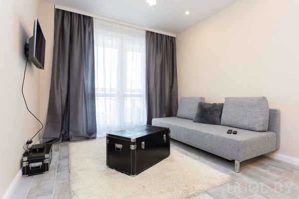 Комната с диваном, столом, телевизором, тюлем, шторами и светлой плиткой на полу.