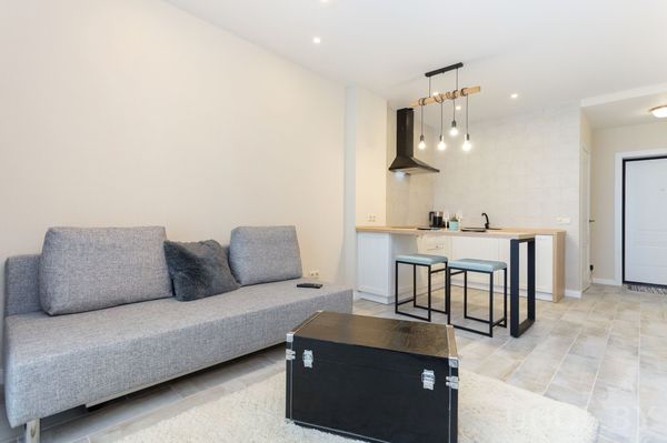 Композиция с диваном, столом, барными стульями, подвесными лампами и светлой плиткой.