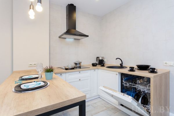 Рабочая зона с деревянной столешницей, белыми фасадами, чёрной техникой, посудой и подвесным светом.