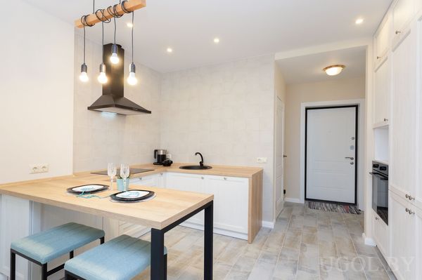 Интерьер с белыми фасадами, деревянной столешницей, синими стульями, плиткой и подвесными лампами.