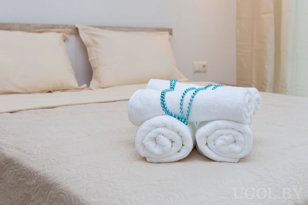 Кровать с бежевым текстилем, декоративной композицией из полотенец и бирюзовыми бусами.