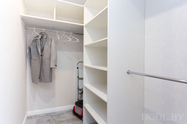 Зона хранения с полками, вешалками, стремянкой, ящиком и светлой плиткой.