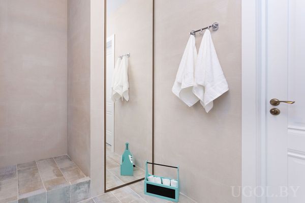 Композиция с зеркалом, полотенцами, корзиной, бутылкой, дверью и светлой плиткой.